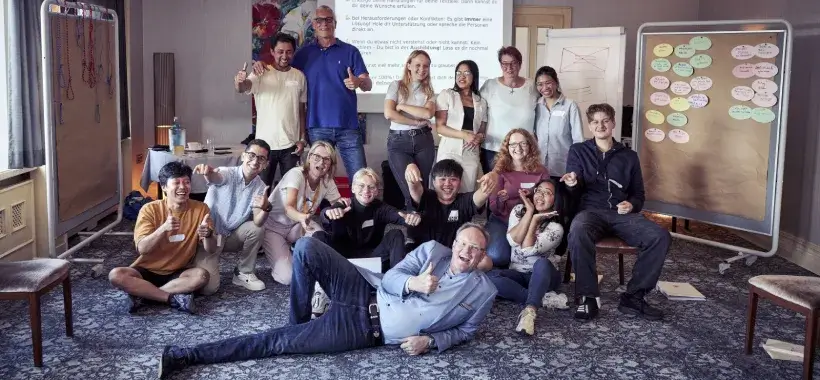 Eine Gruppe von Workshop-Teilnehmern posiert lächelnd in einem Seminarraum mit Flipcharts im Hintergrund.